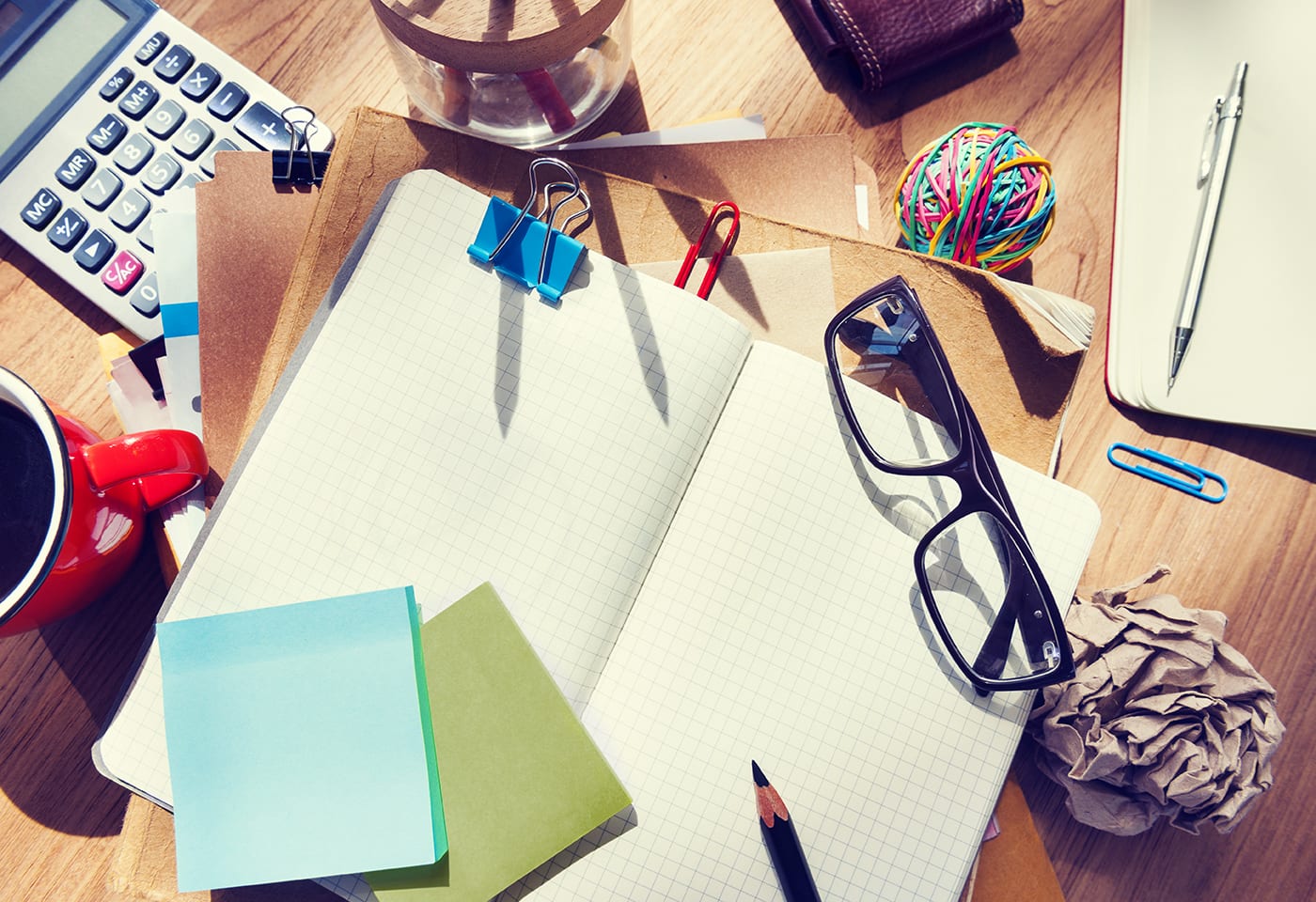 a messy desk with notebooks, glasses, a calculator and other items