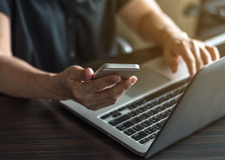 hands on a laptop keyboard holding a mobile phone