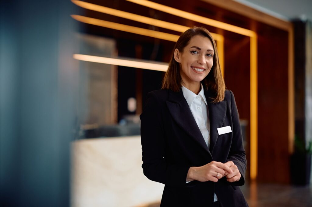 Happy female concierge in hotel hallway looking at camera.